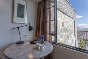 Una habitación con una mesa de mármol, un cuadro enmarco, una lámpara y un ventanal con vista a un edificio de piedra.