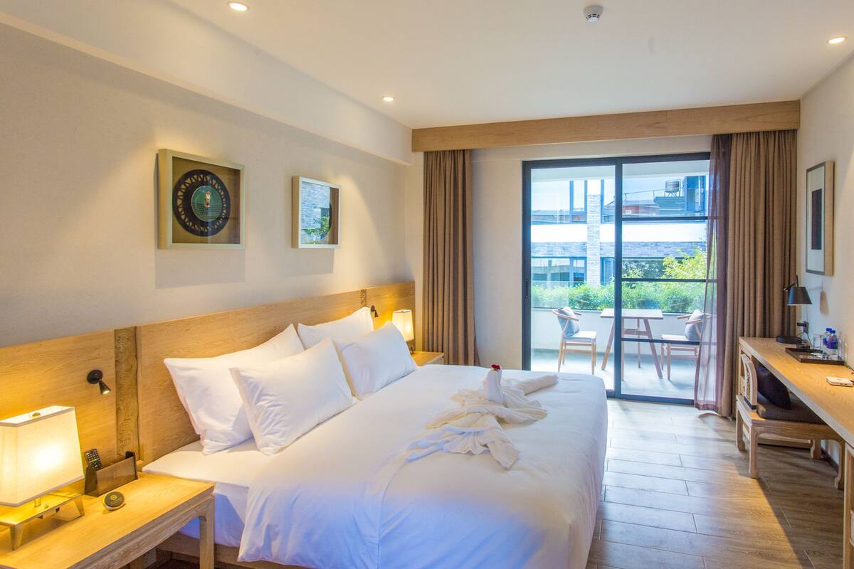 Habitación de hotel con una cama grande, un escritorio y un balcón con mobiliario exterior.