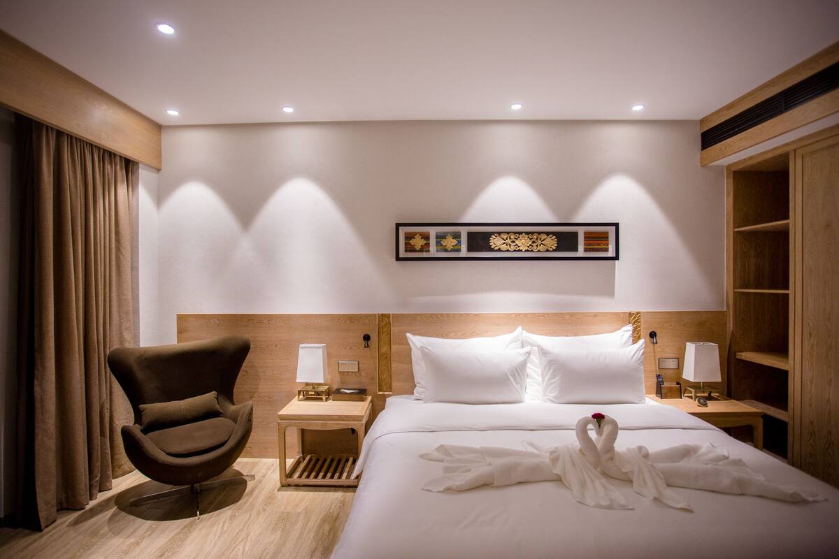 Una habitación de hotel con una cama, una silla, una mesita de noche y una obra de arte colgada en la pared.