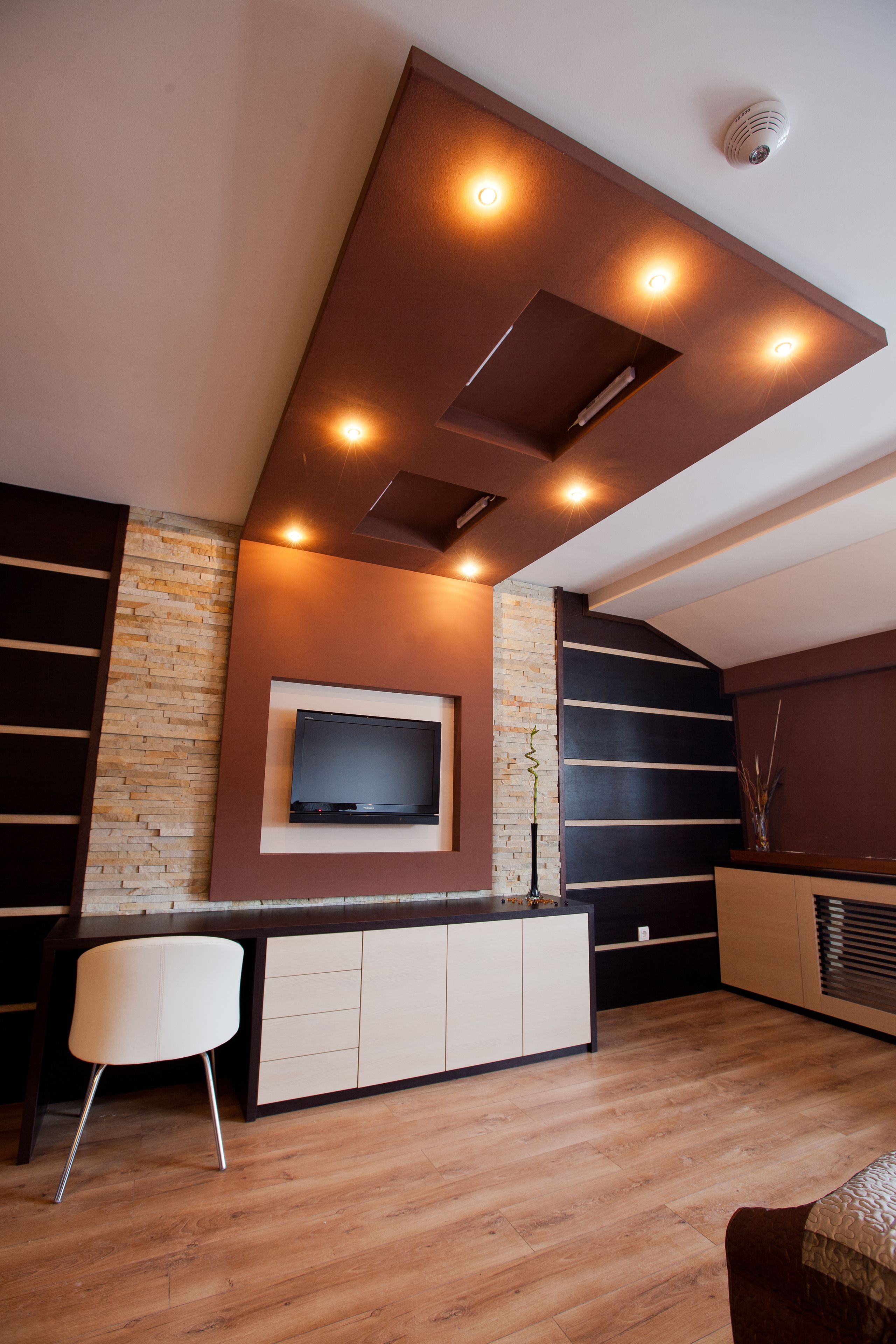A modern living room with a built-in TV, wooden flooring, and a seating area with a white chair.