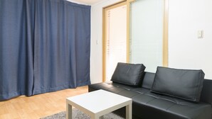 A living room with a black leather sofa, a white coffee table, and a blue curtain. - Seoul Galleria (Seoul)