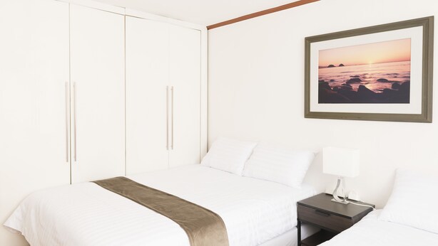 A neatly made bed with a white comforter and a brown throw blanket, a bedside table with a lamp, and a framed picture of a sunset over the ocean on the wall. - Seoul Galleria (Seoul)