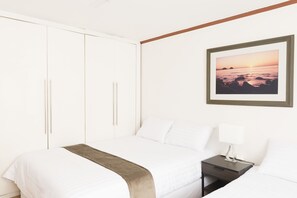 A neatly made bed with a white comforter and a brown throw blanket, a bedside table with a lamp, and a framed picture of a sunset over the ocean on the wall. - Seoul Galleria (Seoul)