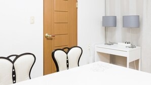 A room with a wooden door, white walls, a white table with a floral design, two chairs with black frames, and a white desk with two lamps. - Seoul Galleria (Seoul)
