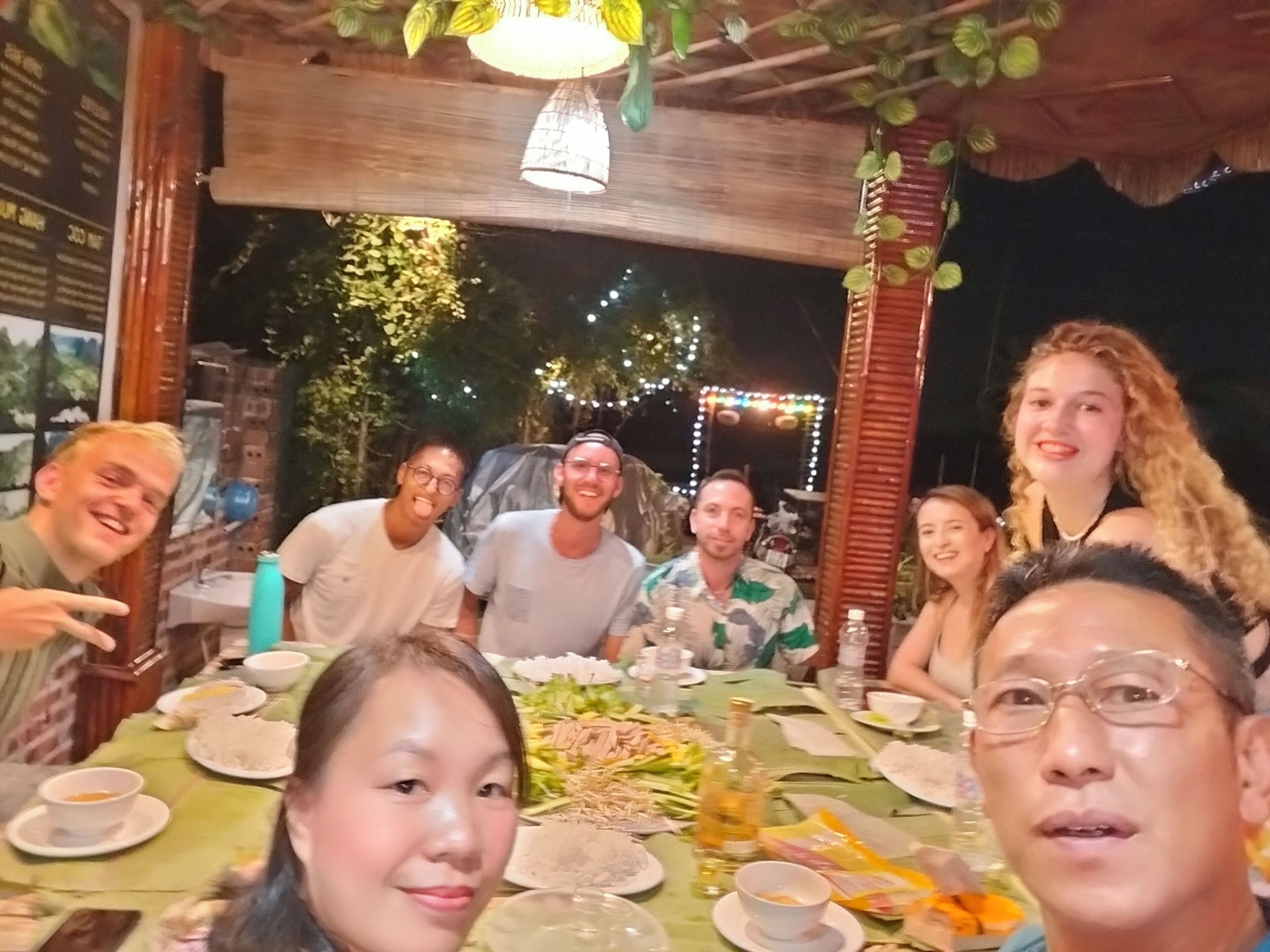 Un grupo de personas sentadas alrededor de una mesa con diferentes platos y una botella de vino.