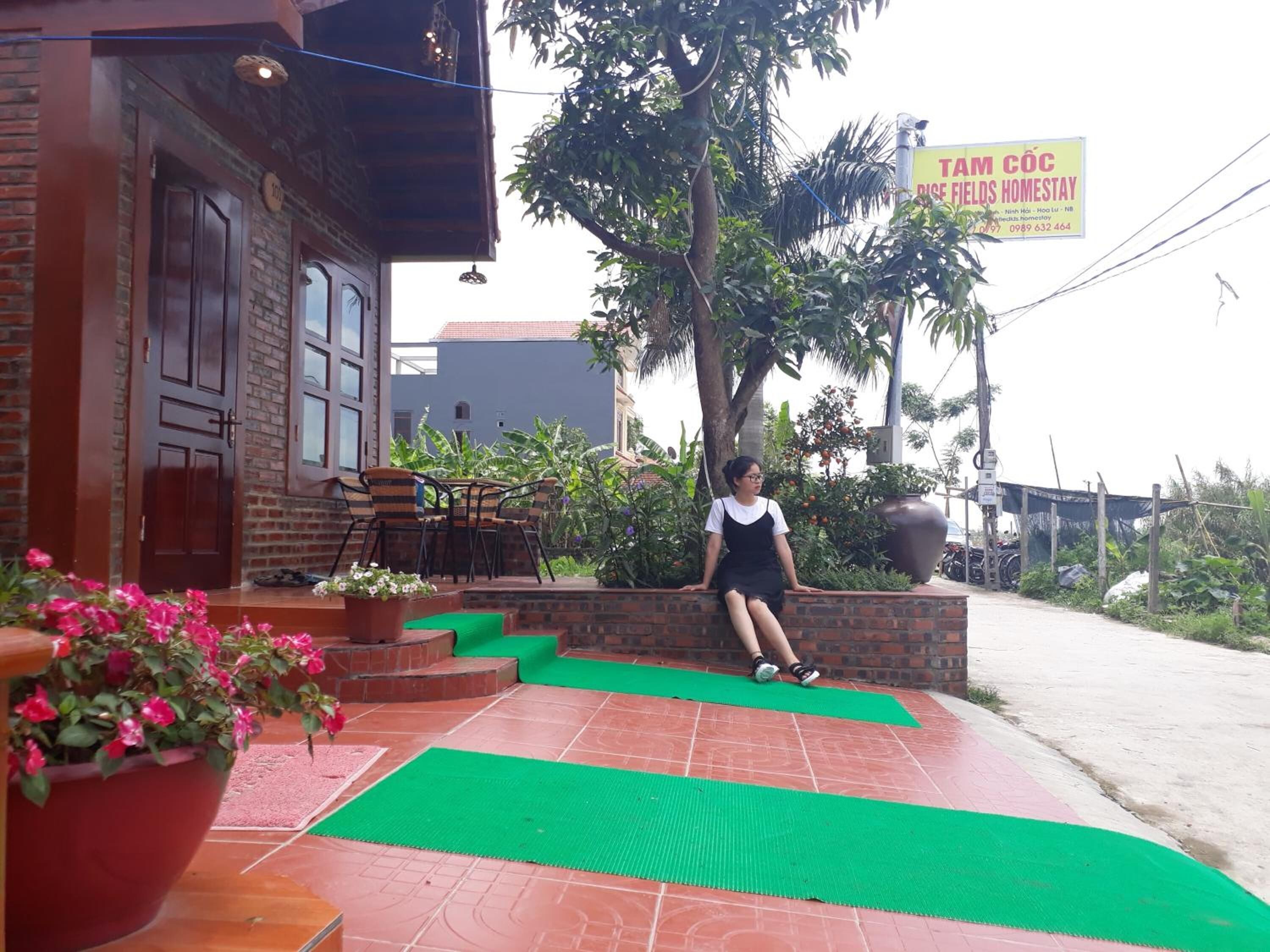 A person sitting on a brick ledge outside a building with a signboard in the background.