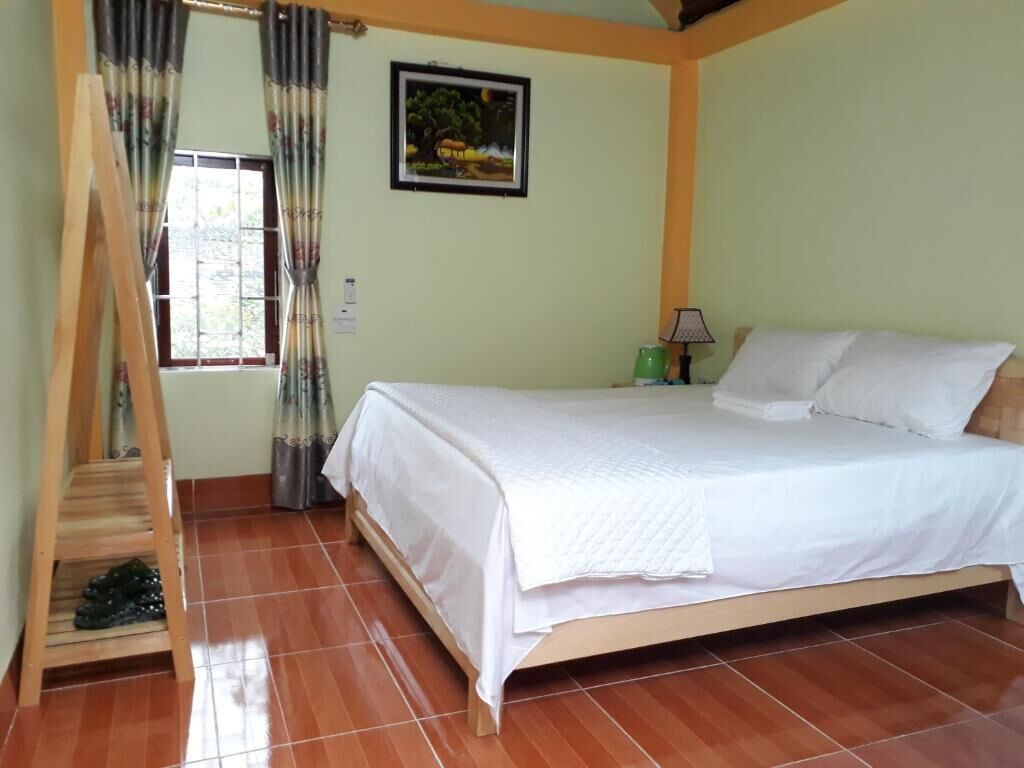 Un dormitorio con cama, ventana con cortinas, un cuadro en la pared y una escalera de madera.