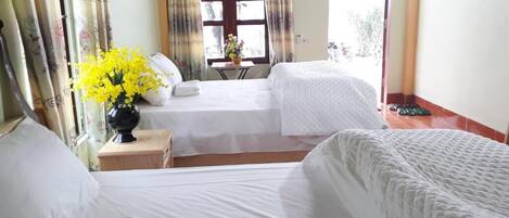 Une chambre d’hôtel avec deux lits, une petite table ornée d’un vase de fleurs et une fenêtre avec des rideaux.