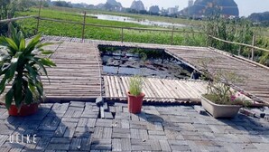 A rooftop terrace with a small pond, potted plants, and a view of a distant landscape with water and hills. - Tam Coc Rice Fields Homestay (Nam Hoa Lu)