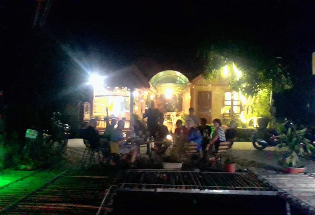 An outdoor seating area with tables and chairs, surrounded by potted plants and a building with a dome-shaped roof.