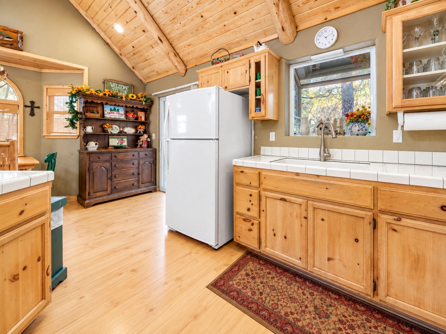 Una cocina con armarios de madera, un refrigerador blanco y una ventana con vista a árboles.