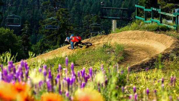 Ciclista de montanha numa pista de terra, com um teleférico ao fundo.