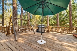 Een houten terras met een schommel, een barbecue en een groene parasol.