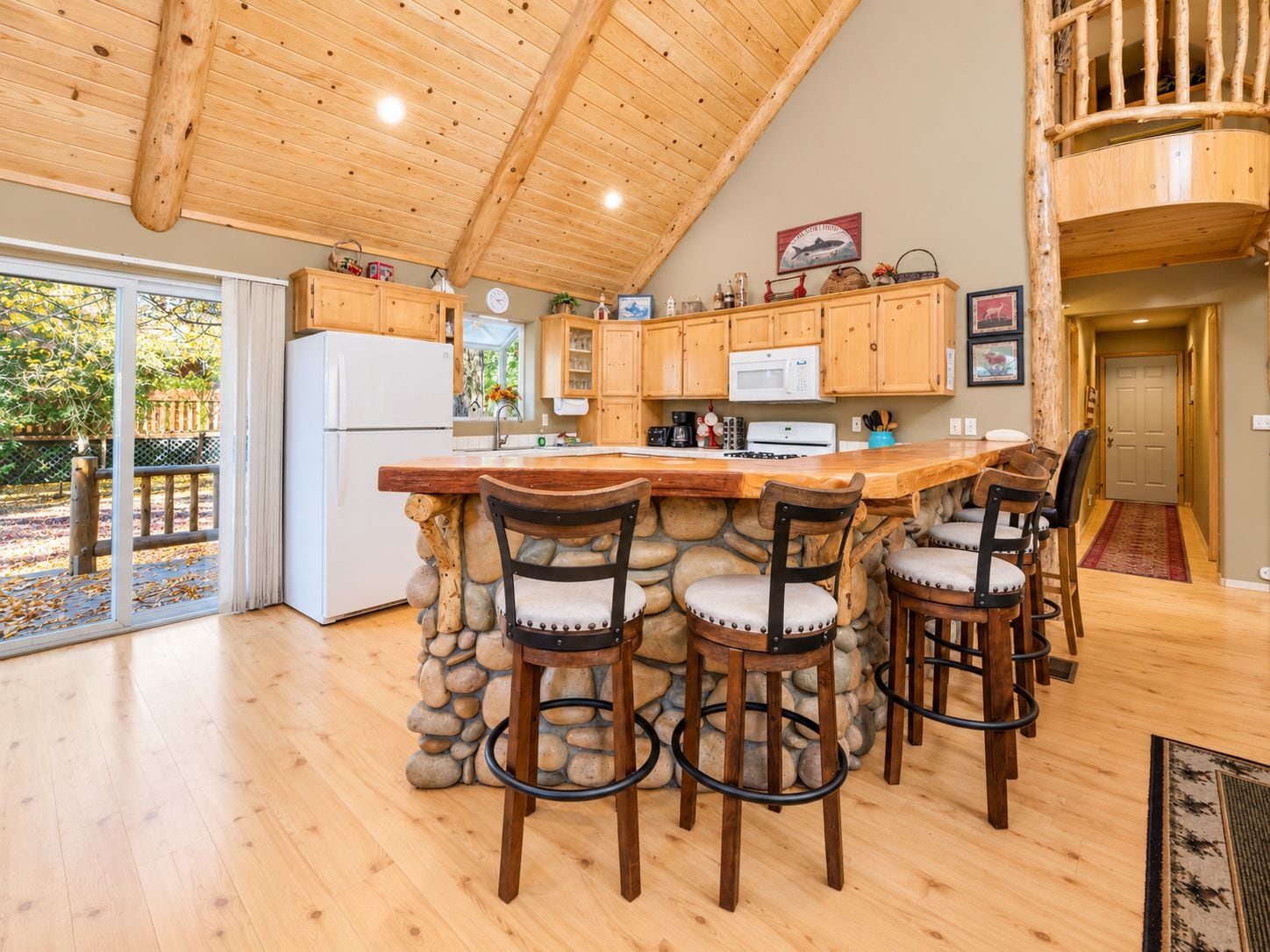 Una cocina con una isla de piedra, sillas de madera y un refrigerador blanco.