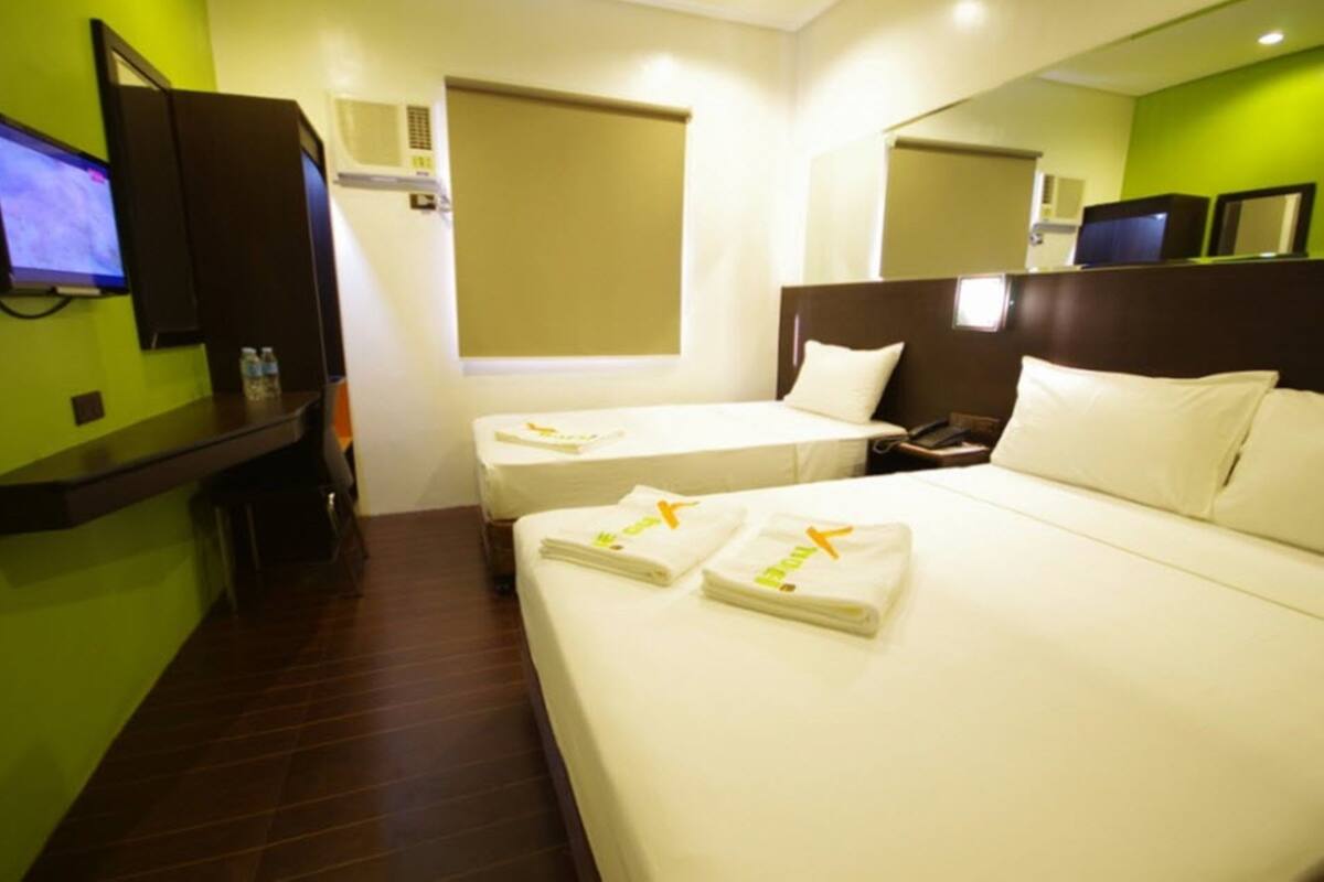 A hotel room with a large bed, a smaller bed, a desk with a computer, and a television on the wall.
