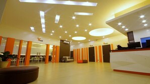 Ett modernt receptionsområde med en vit receptionsdisk, orange detaljer och en sittgrupp med en brun pall.