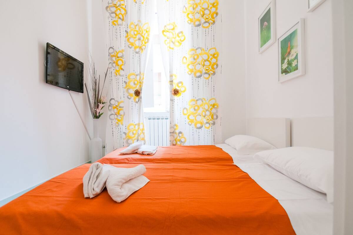 A hotel room with a bed, a TV mounted on the wall, and a window with curtains.