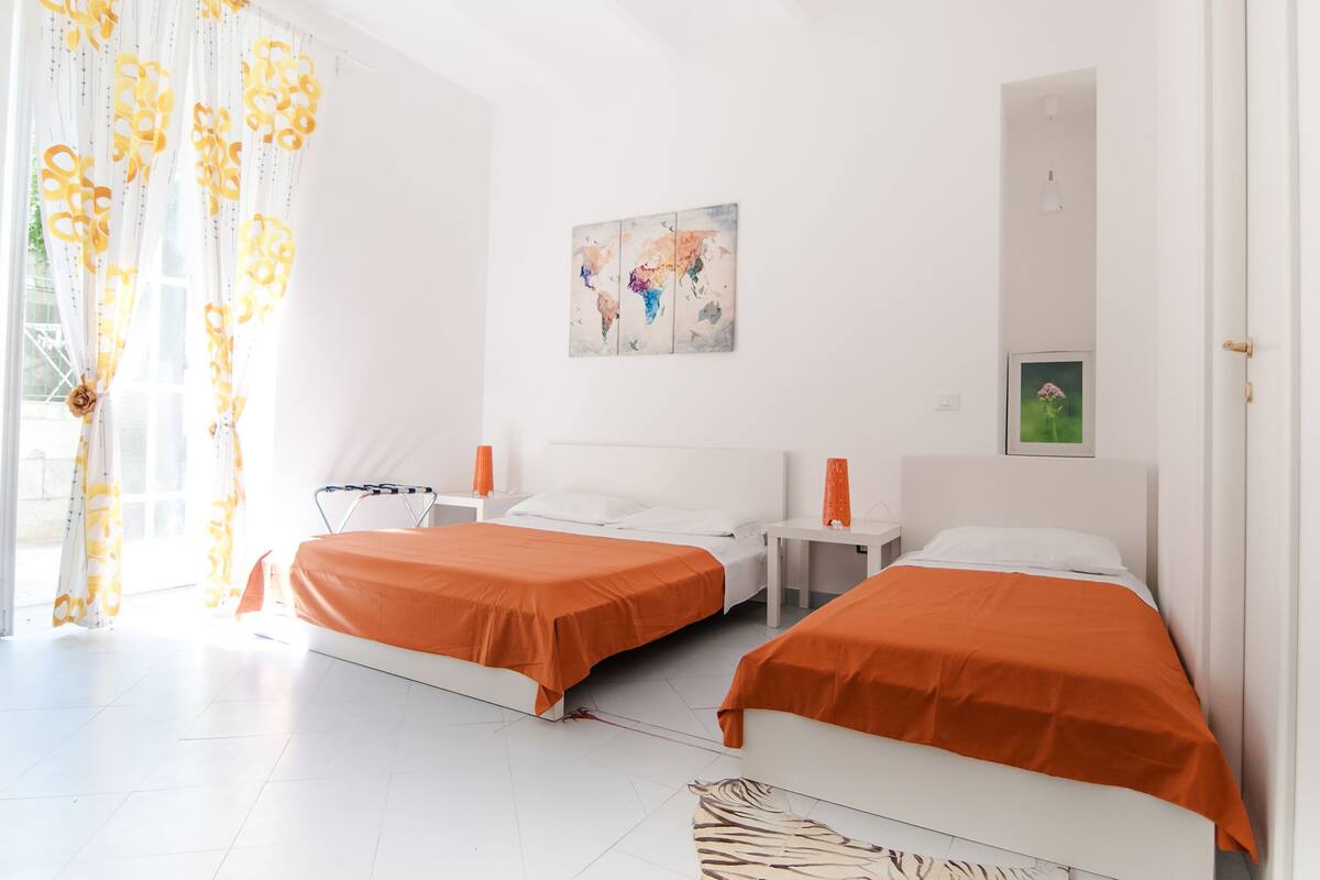 A hotel room with two beds, white walls, a painting, and a window with curtains.