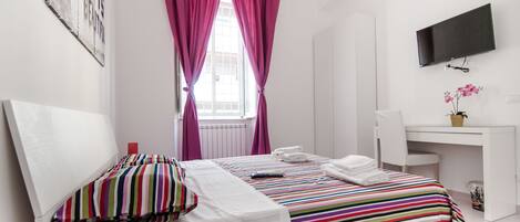 Una habitación de hotel con cama, escritorio, televisor y ventana con cortinas.