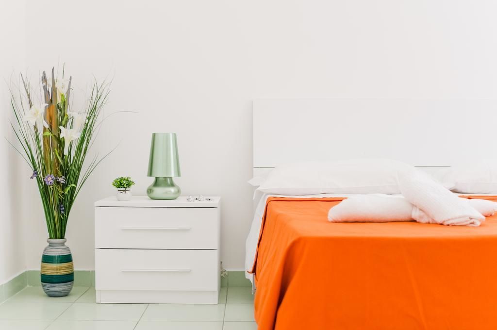A hotel room with a bed, a nightstand, a lamp, and a vase with flowers.