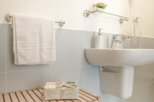 A bathroom with a white sink, a towel hanging on a rack, and a small wooden bench with a decorative box. - Speciale Guesthouse (Rome)