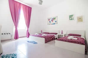 A bedroom with two beds, pink curtains, a world map artwork, and a small table with a lamp. - Speciale Guesthouse (Rome)