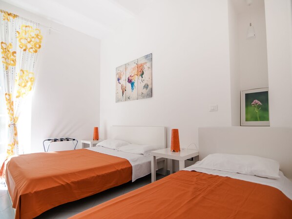 Quarto de hotel com duas camas, uma mesinha de cabeceira, um abajur e um quadro na parede.