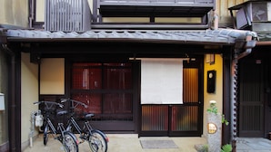 A traditional Japanese building with a tiled roof, a black gate, and a stone lantern. - Kyo Akari Inn (Kyoto)