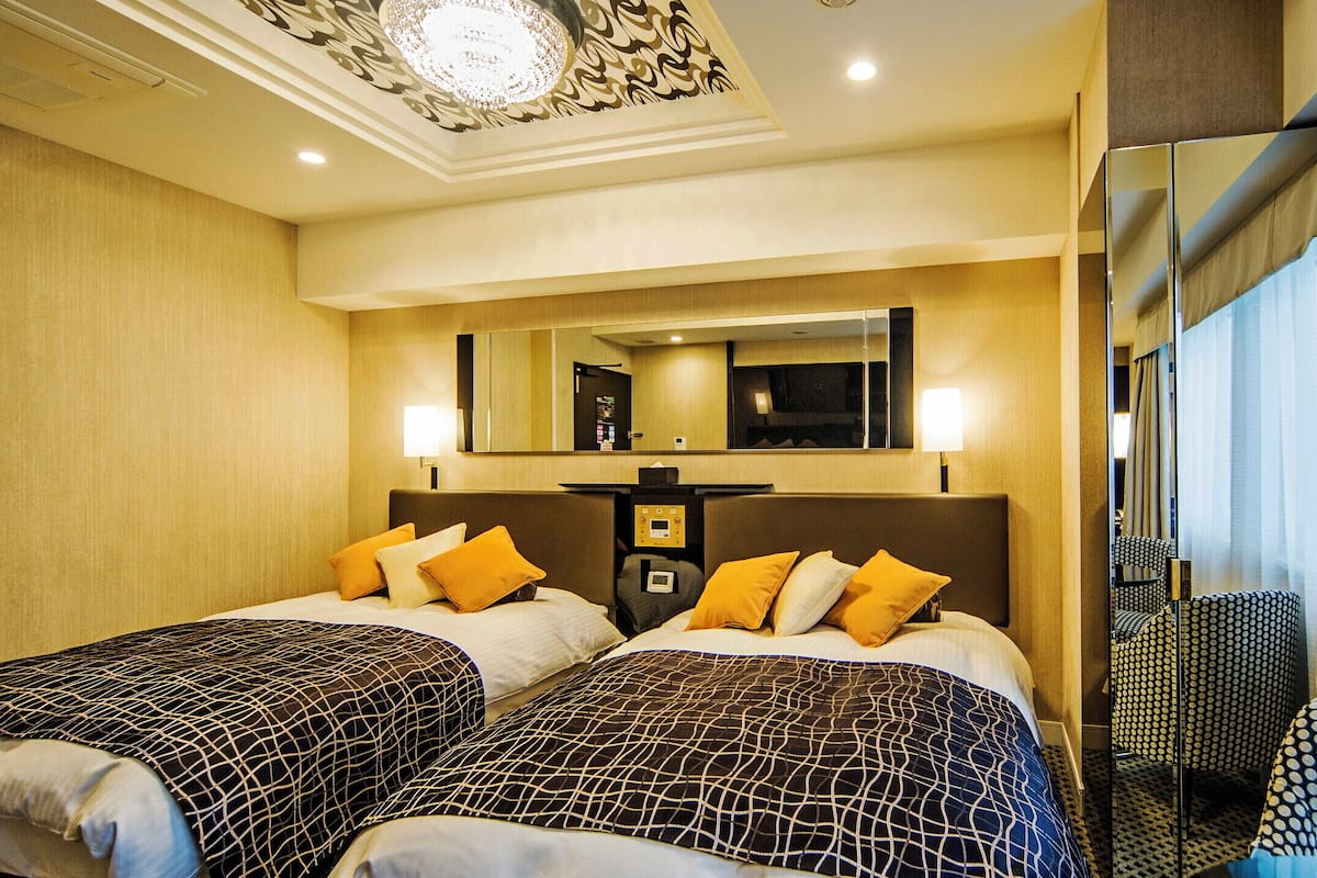 Ein Hotelzimmer mit zwei Betten, einem großen Spiegel, einer Steuerung und Blick auf die Stadt.