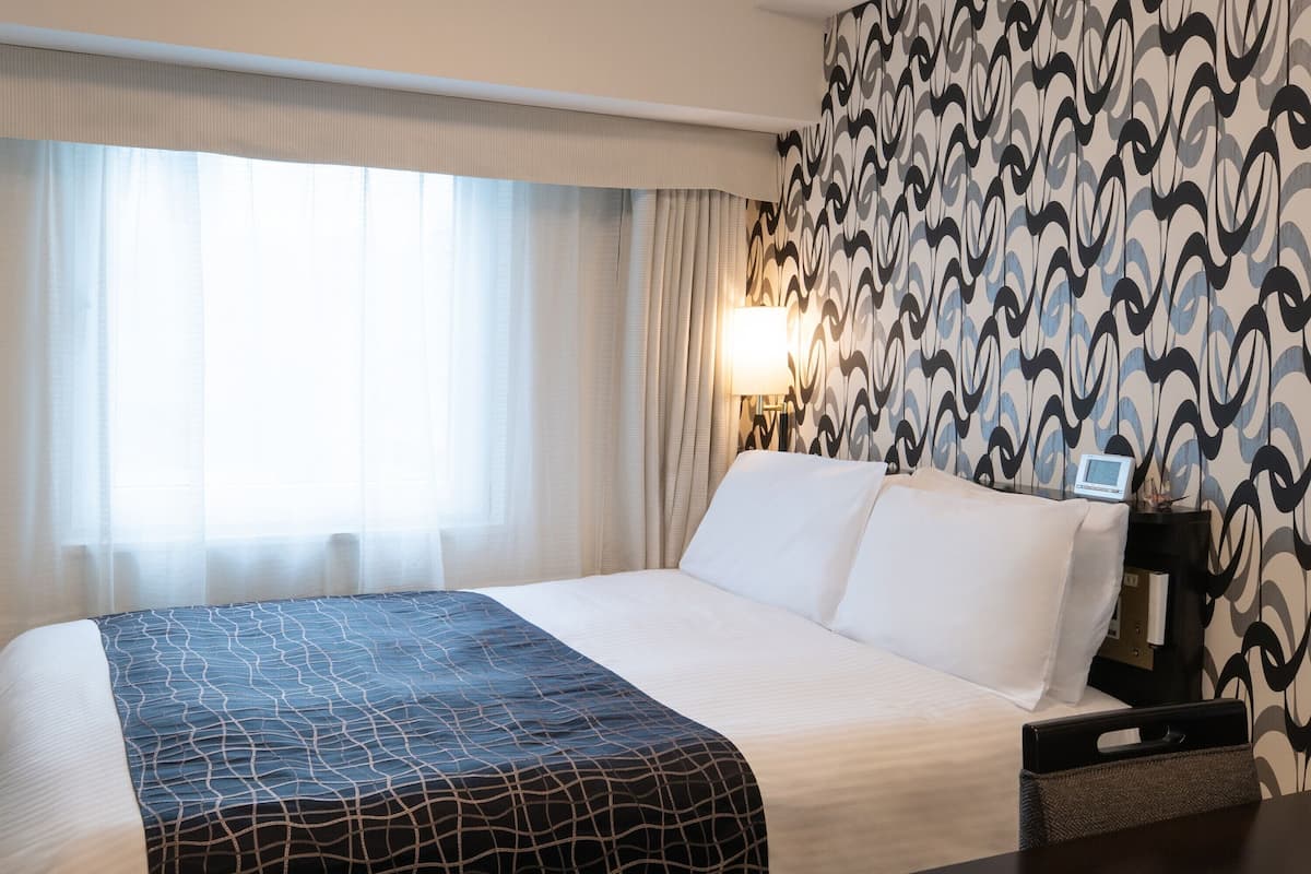 Ein Hotelzimmer mit einem großen Bett, einem Nachttisch mit Lampe und einer Wand mit Muster.