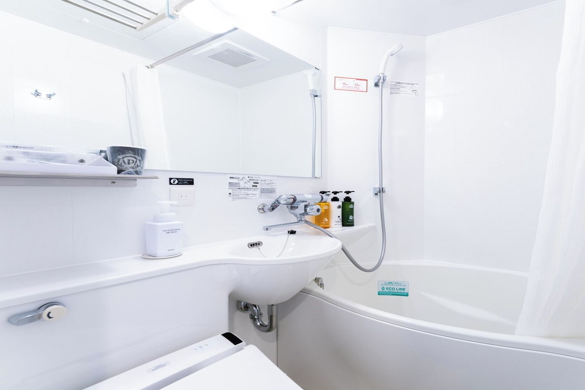 A modern bathroom with a sink, mirror, shower, and toiletries.