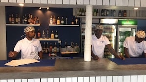 Zona de bar con estantes llenos de botellas de licor, un refrigerador y una barra con un menú.