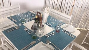 Una mesa para cuatro con sillas blancas, mantel azul y diverso juego de copas y cubiertos.