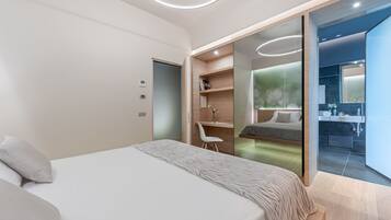 Camera da letto moderna con un letto grande, una scrivania e un bagno visibile attraverso una porta in vetro.