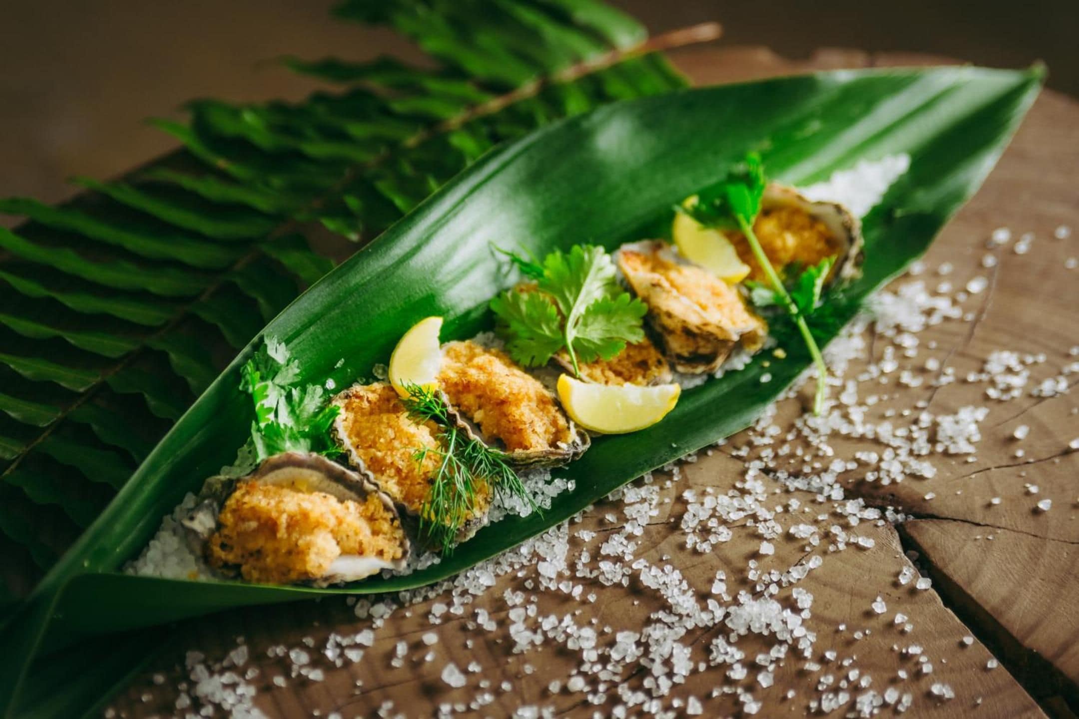 A dish of breaded and fried food items served on a green leaf with lemon wedges and herbs.