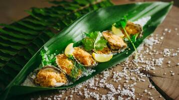 A dish of breaded and fried food items served on a green leaf with lemon wedges and herbs.