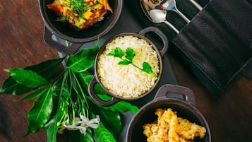 Une table avec quatre récipients noirs contenant différents plats, une serviette noire avec des couverts, et une plante aux feuilles vertes.