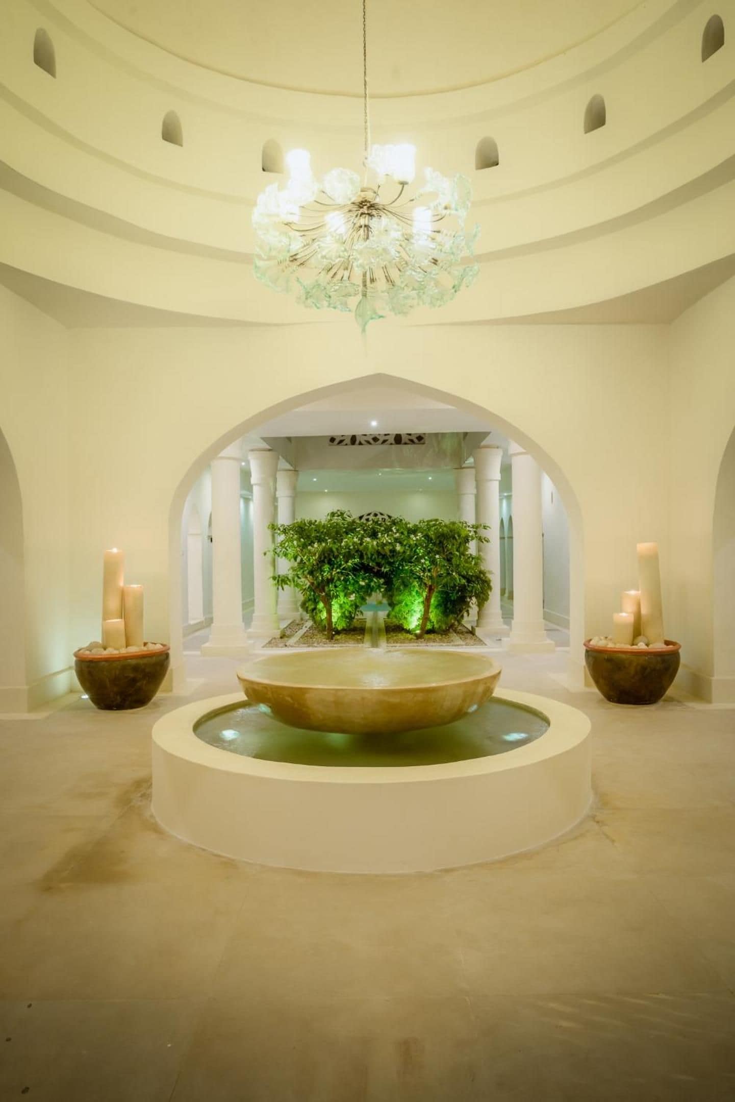Una fuente circular con un elemento central de agua, flanqueada por dos macetas y dos velas.