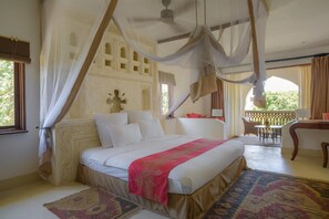 A bedroom with a large bed, a canopy, a balcony with a table and chairs, and a view of greenery outside. - Swahili Beach Resort (Diani Beach)