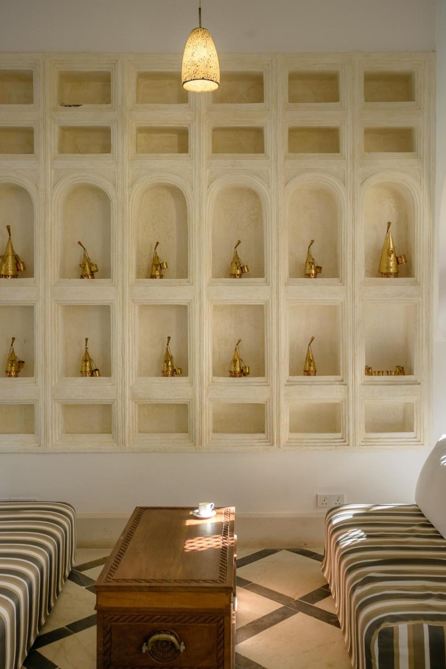 Una habitación con un estante de pared exhibiendo objetos decorativos, una mesa de madera y asientos tapizados a rayas.