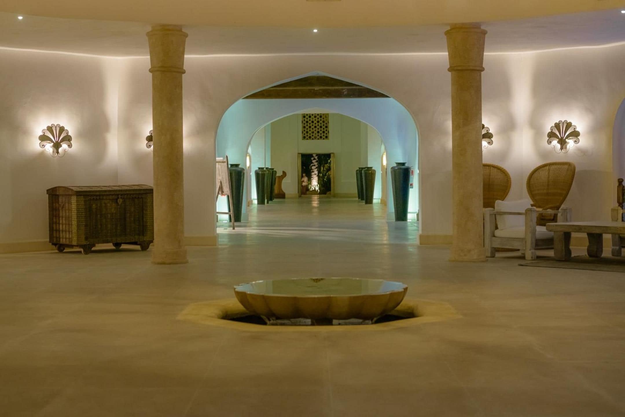 A spacious lobby with a central fountain, columns, and a view into a room with a large vase.