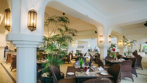 A spacious restaurant with high ceilings, arched columns, and wicker furniture. Tables are set with plates, cutlery, and glasses. - Swahili Beach Resort (Diani Beach)