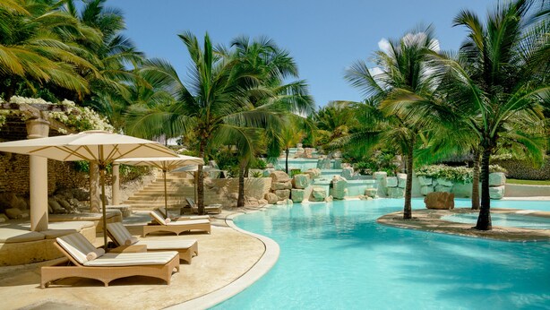 A pool area with lounge chairs and umbrellas, surrounded by palm trees and a stone wall. - Swahili Beach Resort (Diani Beach)