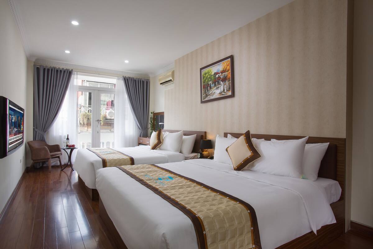 A hotel room with two beds, a sitting area with a chair, a small table, and a window with curtains.