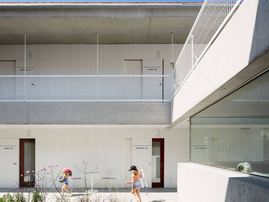 Un bâtiment moderne à la façade en béton, doté d’un balcon avec des balustrades blanches et de deux portes portant les inscriptions « SIMBAD 007 » et « TRAPOBANA 008 ».