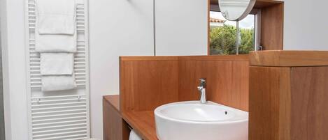 Un baño moderno con tocador de madera, un lavabo blanco, un perchero para toallas y un espejo.