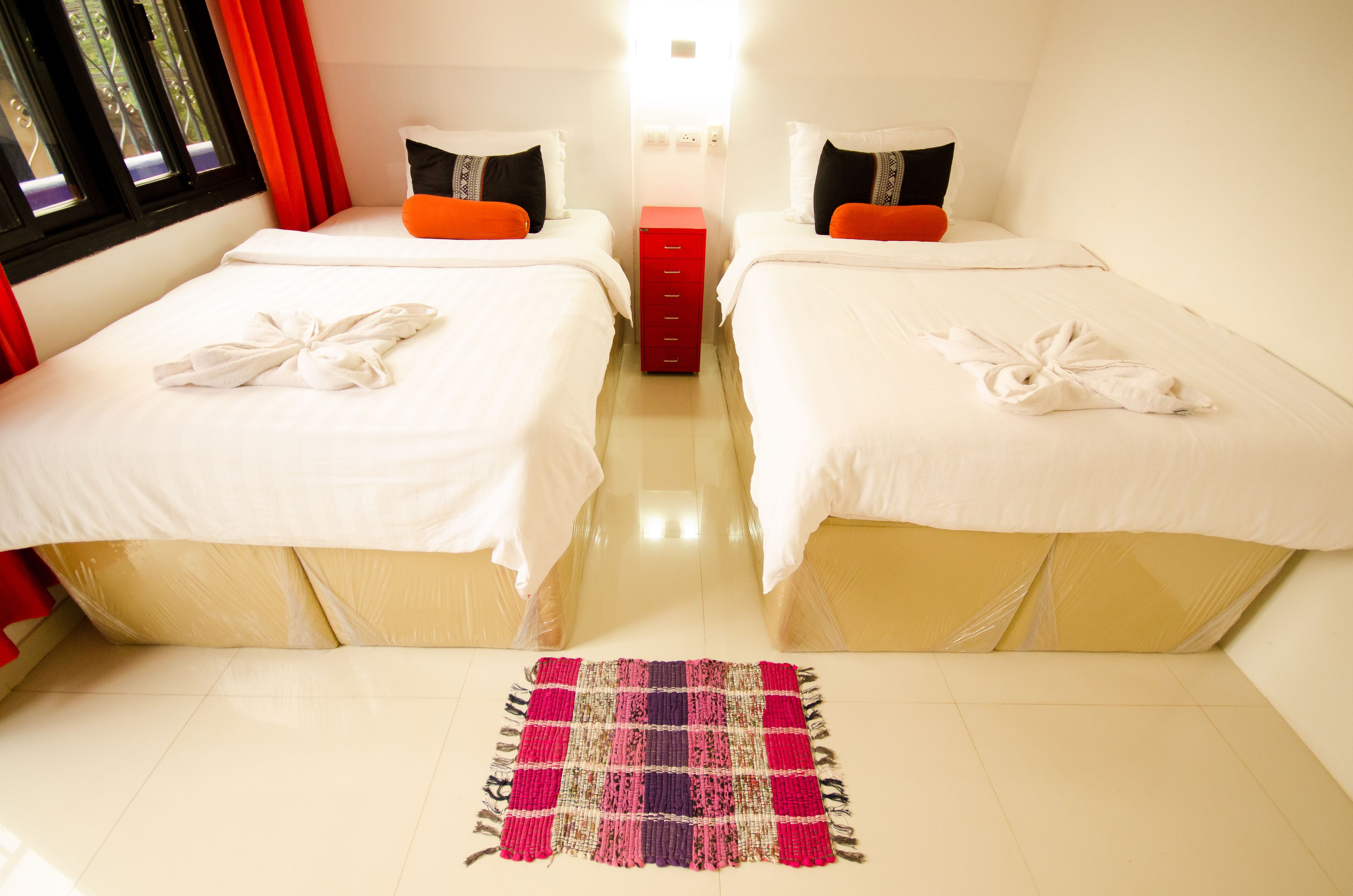 Ein Hotelzimmer mit zwei Betten, einem roten Stauraum und einem farbenfrohen Teppich.