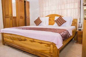 A wooden bed with a headboard, two pillows, and a bedside table with a lamp. - Lovista Hotel (Accra)