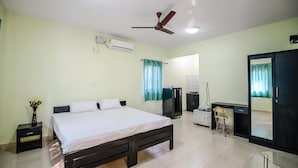 A bedroom with a bed, a desk, a wardrobe, a ceiling fan, an air conditioner, and a mirror. - Sunshine Park Homes (Colva)
