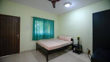 Une chambre à coucher avec un lit, une table de chevet, un ventilateur de plafond et une porte.